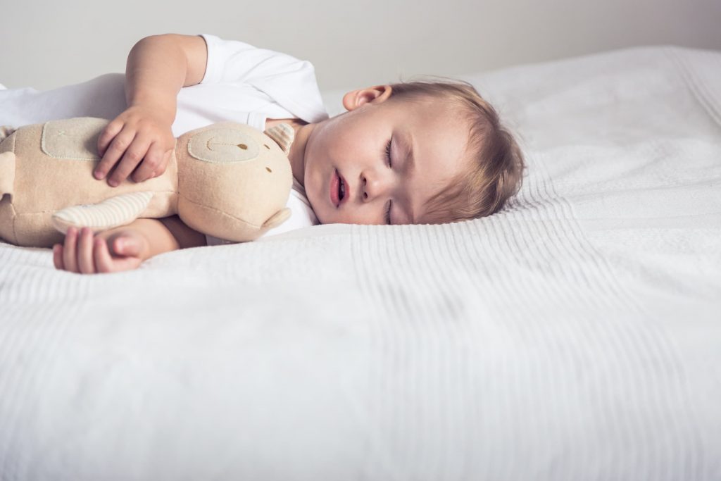 Baby boy sleeping on a bed with teddy bear