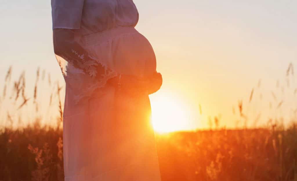 Pregnant woman standing in front of a beautiful sunset