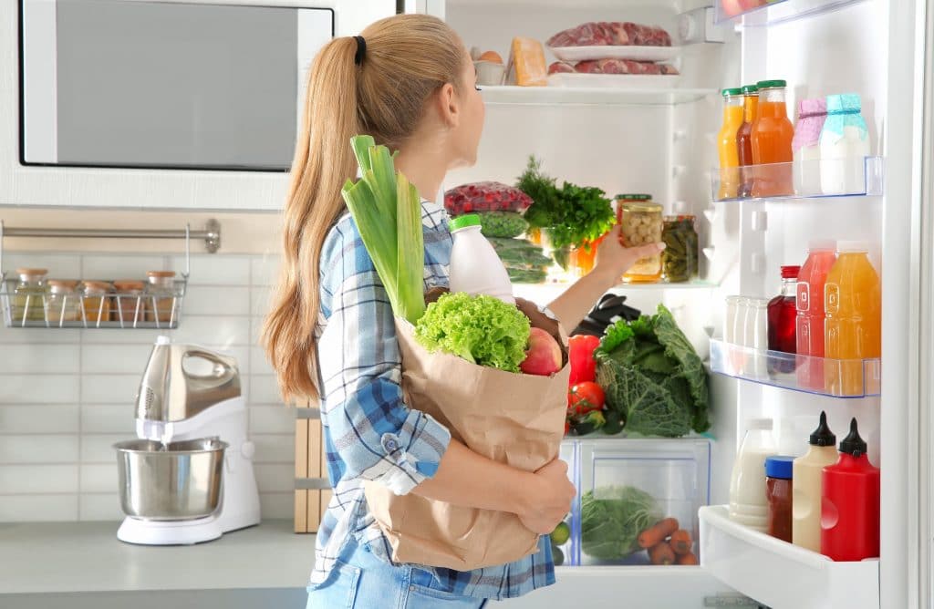 Young woman holding a grocery back, placing groceries into the fridge